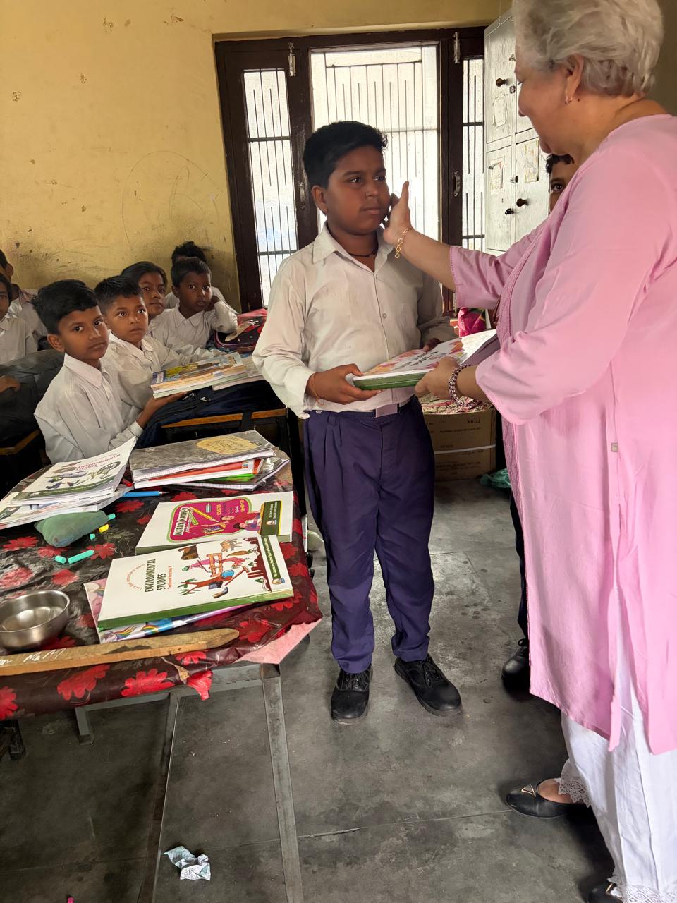 Student receiving books in a classroom with other children seated behind