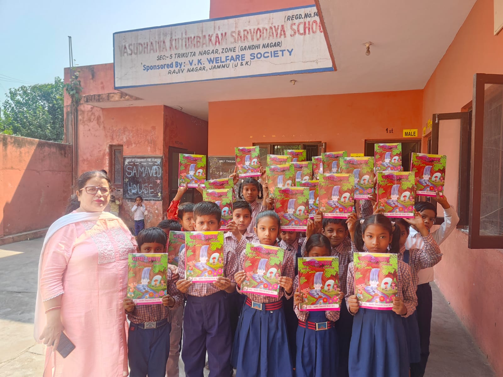 Students holding new books outside a school in Jammu with a TVBT supporter